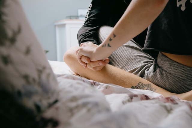 Photo by Sinitta Leunen on UnSplash. Photo of two people holding hands on a bed.